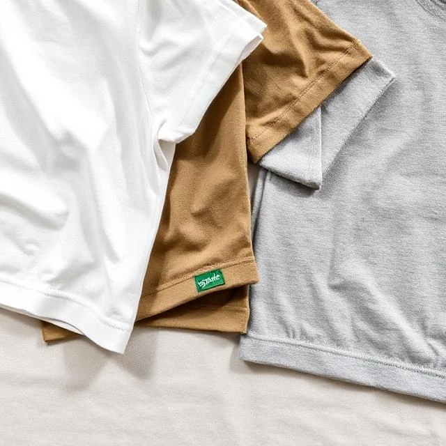 Flat lay of plain eco T-shirts with green woven organic label on hem in white and khaki colors - ethical T-shirt supplier India.